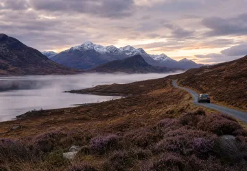 A car travels a scenic mountain road at sunrise.