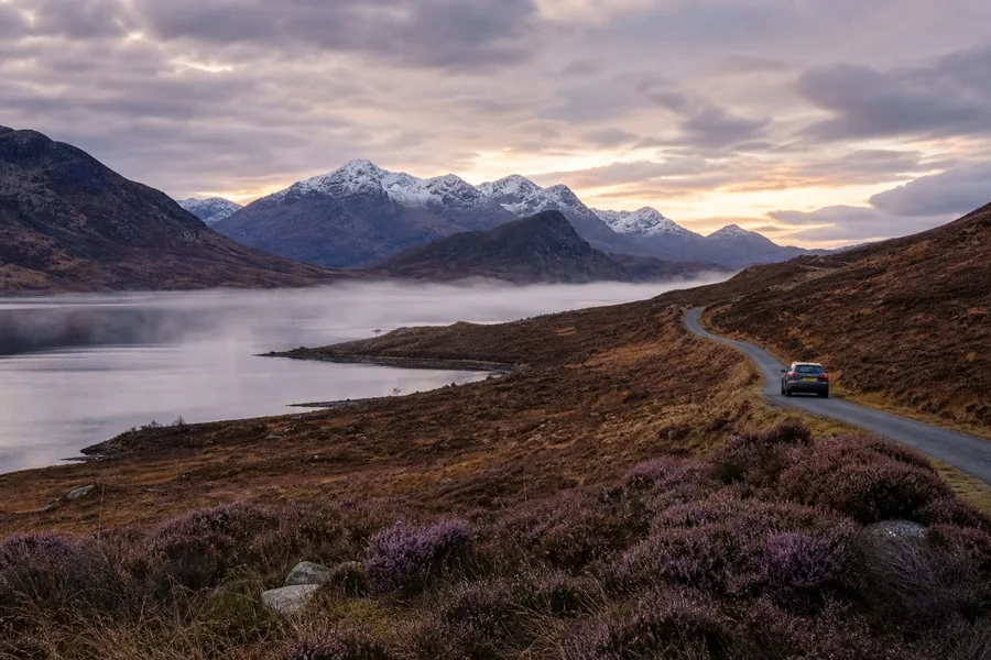 A car travels a scenic mountain road at sunrise.