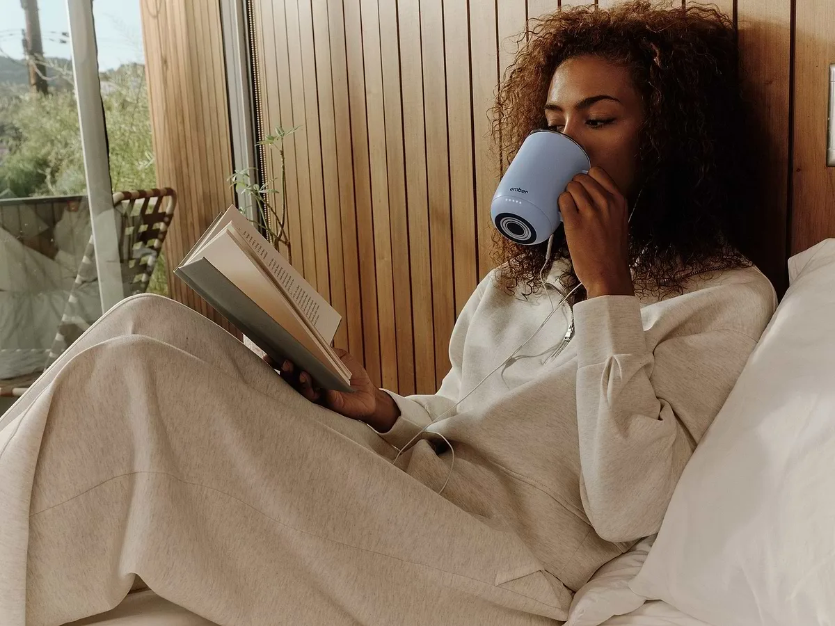 Woman drinking from a powder blue Ember Mug 3 while reading
