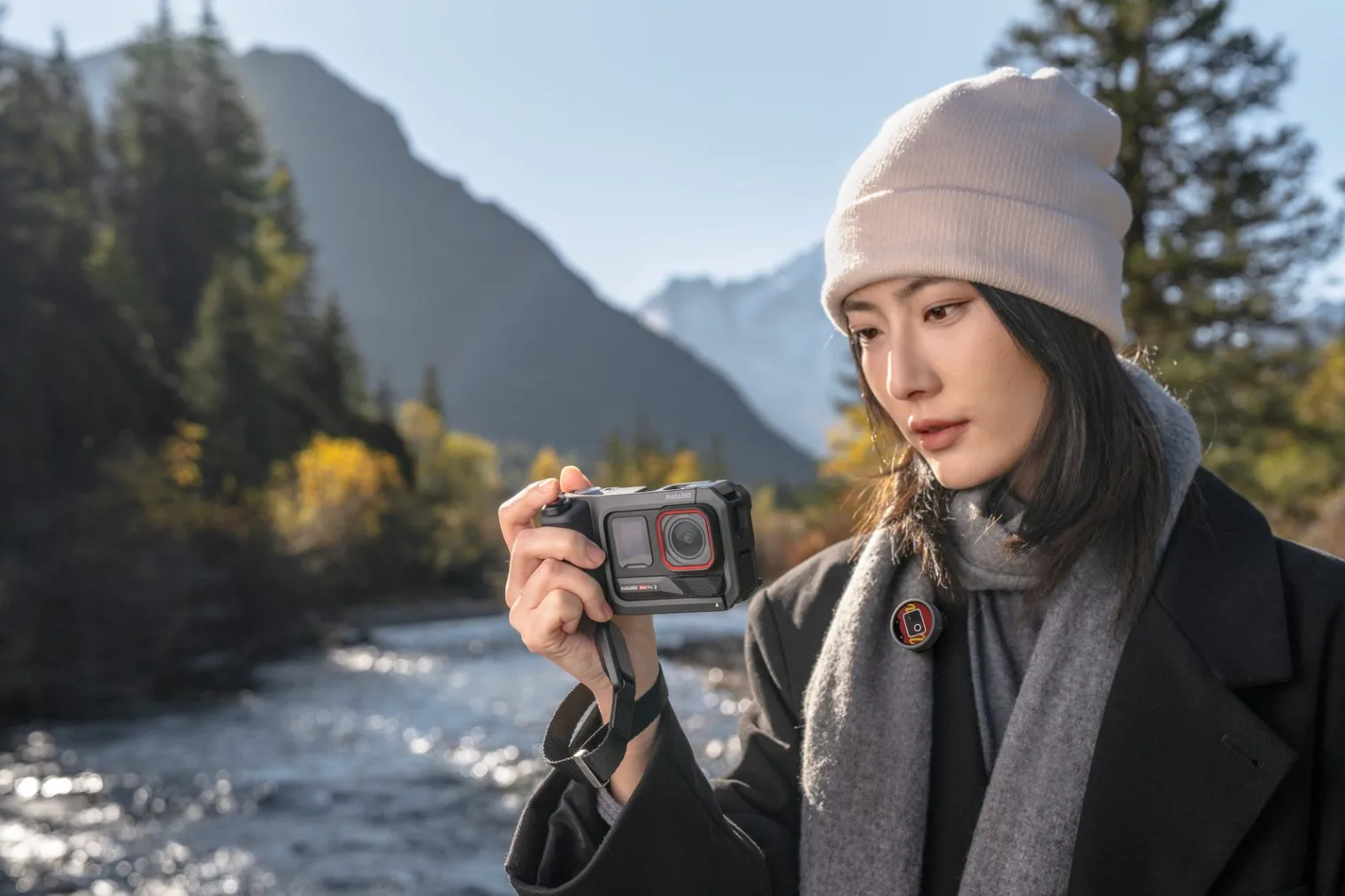 Creator holding Insta360 Ace Pro 2 camera with Insta360 Mic clipped to scarf in mountain valley
