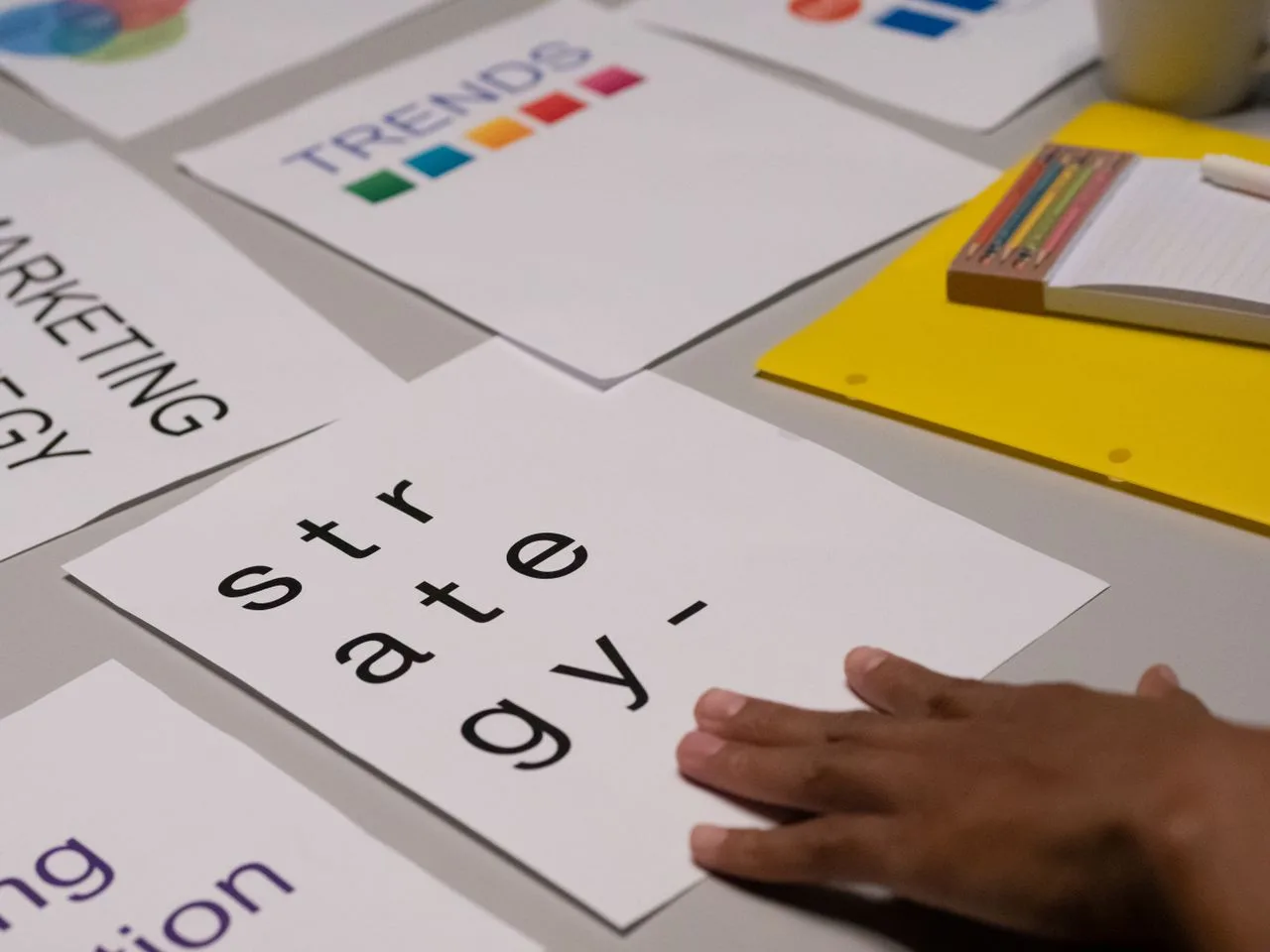 Close-up of marketing strategy notes and a colorful trends sheet on a table for a planning session, with a person's hand on a white paper